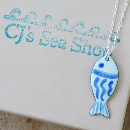 light green and blue enamel fish shaped pendant, displayed on a gift box