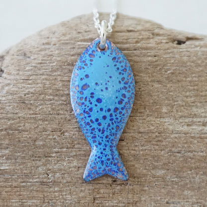 Blue enamel fish shaped pendant against a wooden background