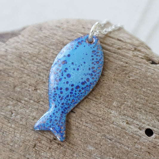 Blue enamel fish shaped pendant against a wooden background