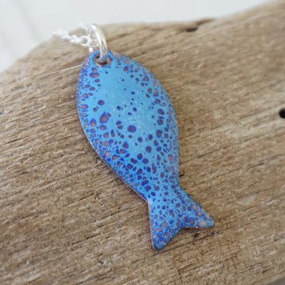 Blue enamel fish shaped pendant against a wooden background