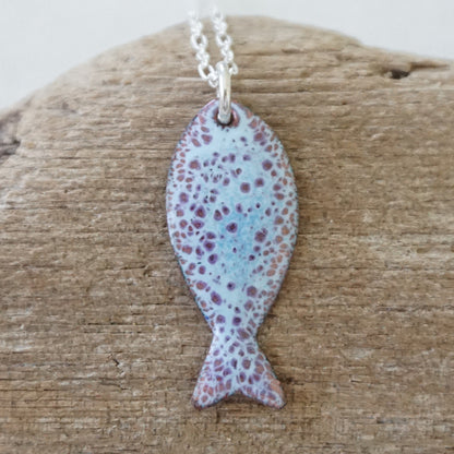 light blue and purple enamel fish shaped pendant against a wooden background