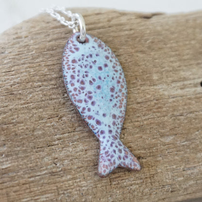 light blue and purple enamel fish shaped pendant against a wooden background