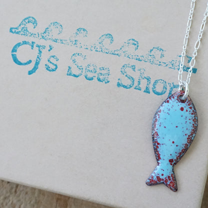 light blue and red enamel fish shaped pendant displayed on a gift box