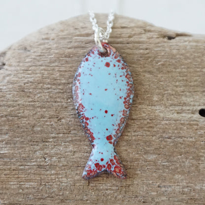 light blue and red enamel fish shaped pendant against a wooden background