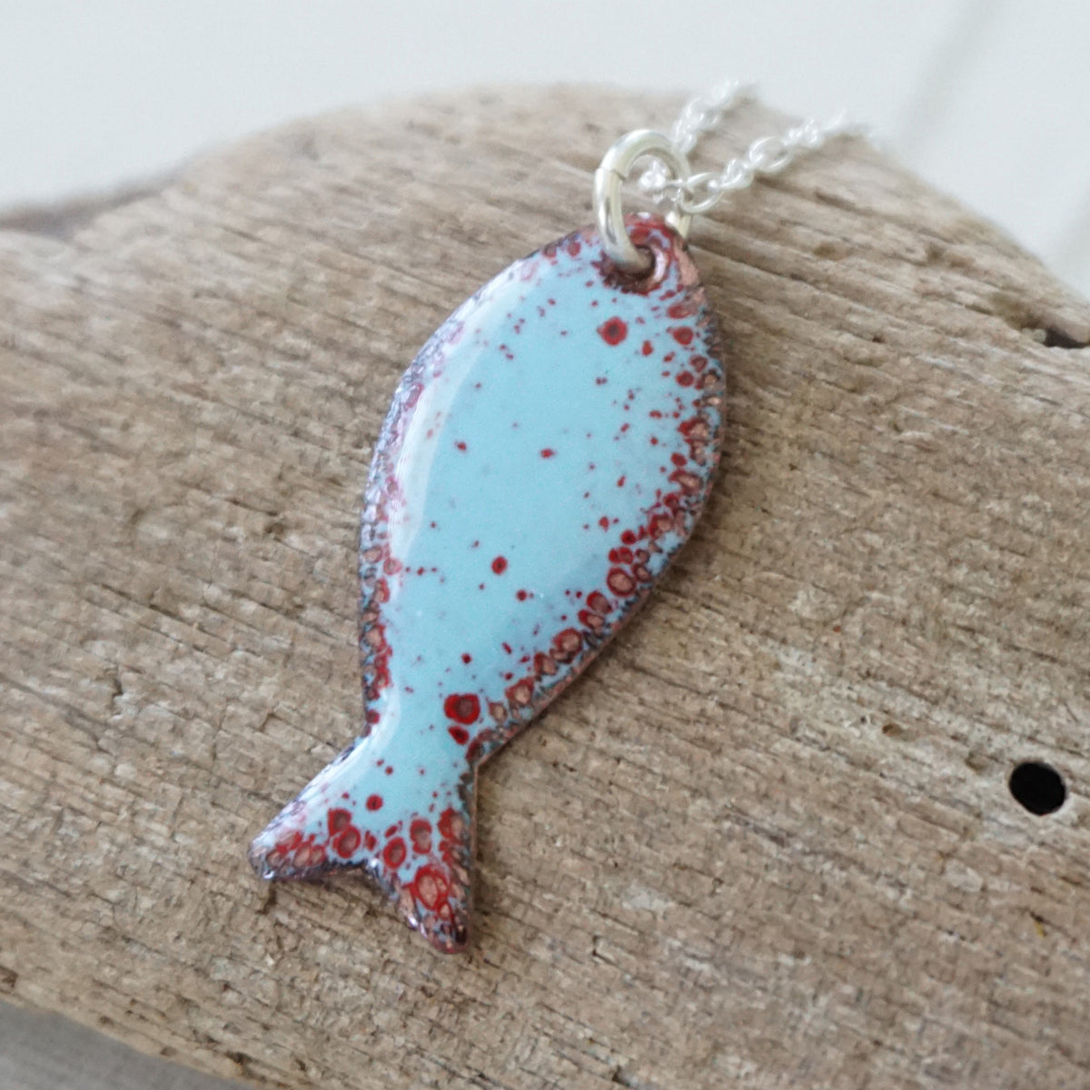 light blue and red enamel fish shaped pendant against a wooden background