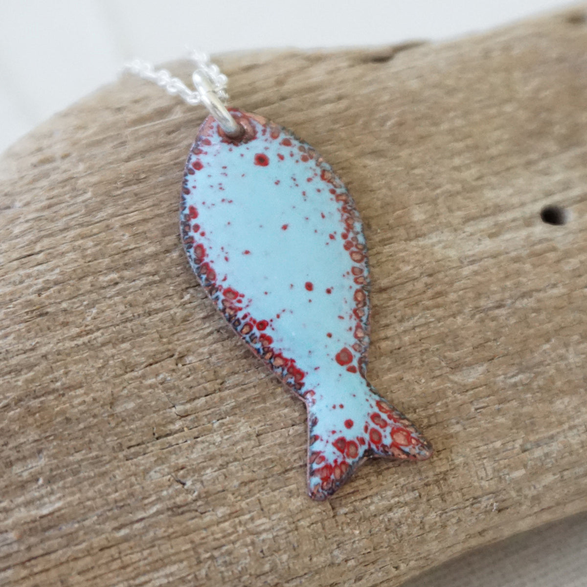 light blue and red enamel fish shaped pendant against a wooden background