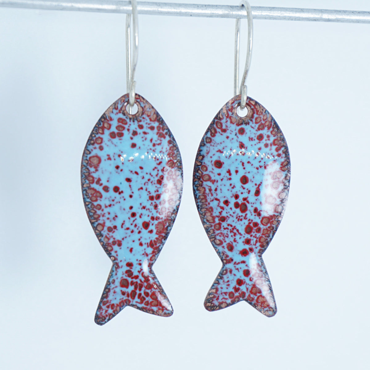 light blue and red enamel fish shaped earrings, against a white background