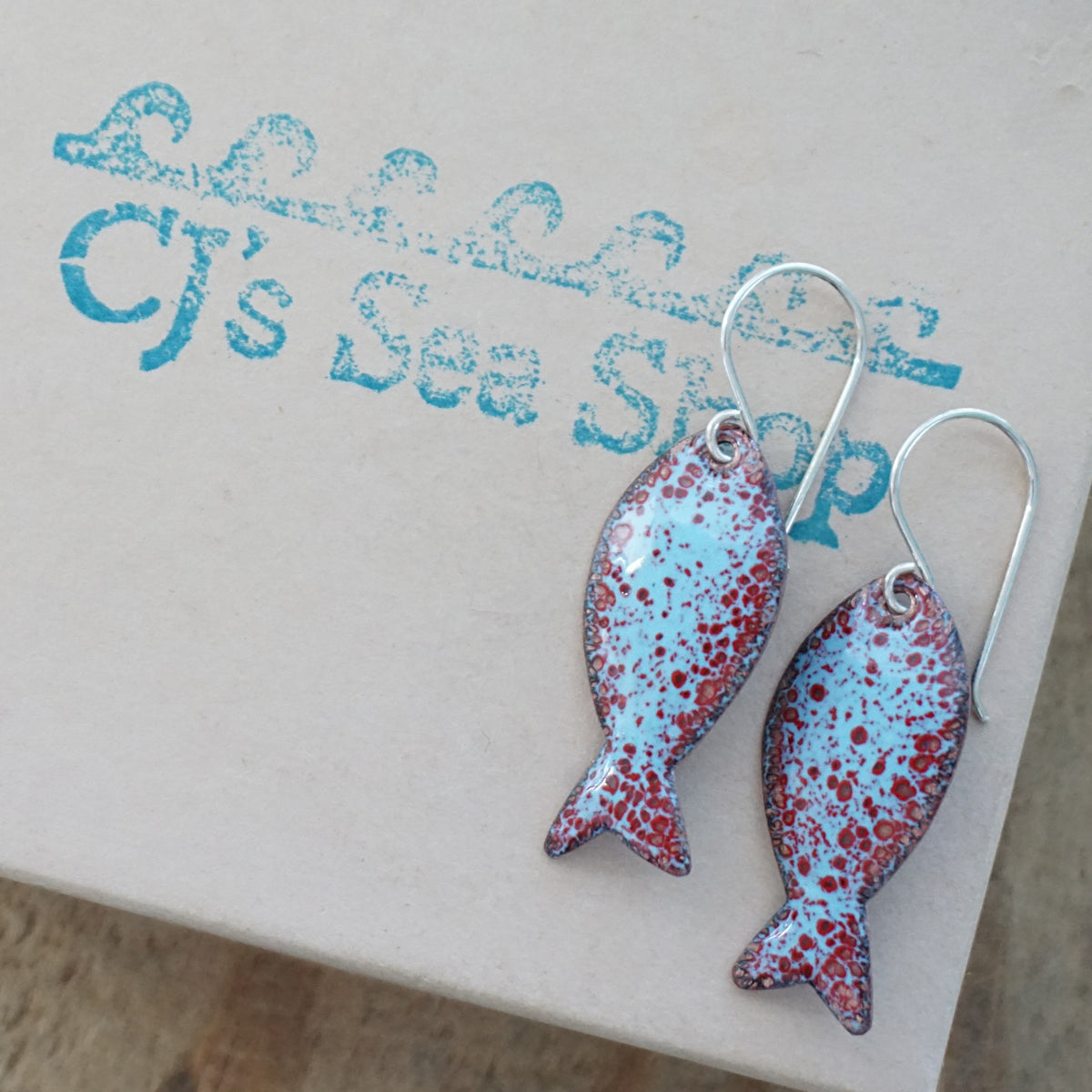 light blue and red enamel fish shaped earrings, displayed on a gift box