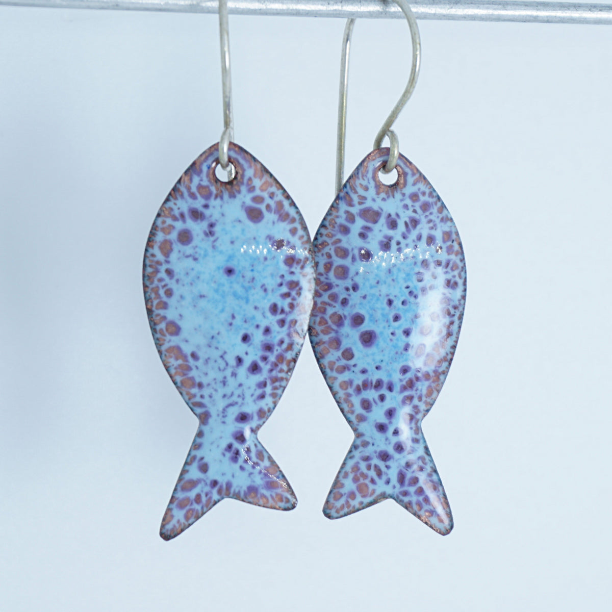 light blue and purple enamel fish shaped earrings, against a white background