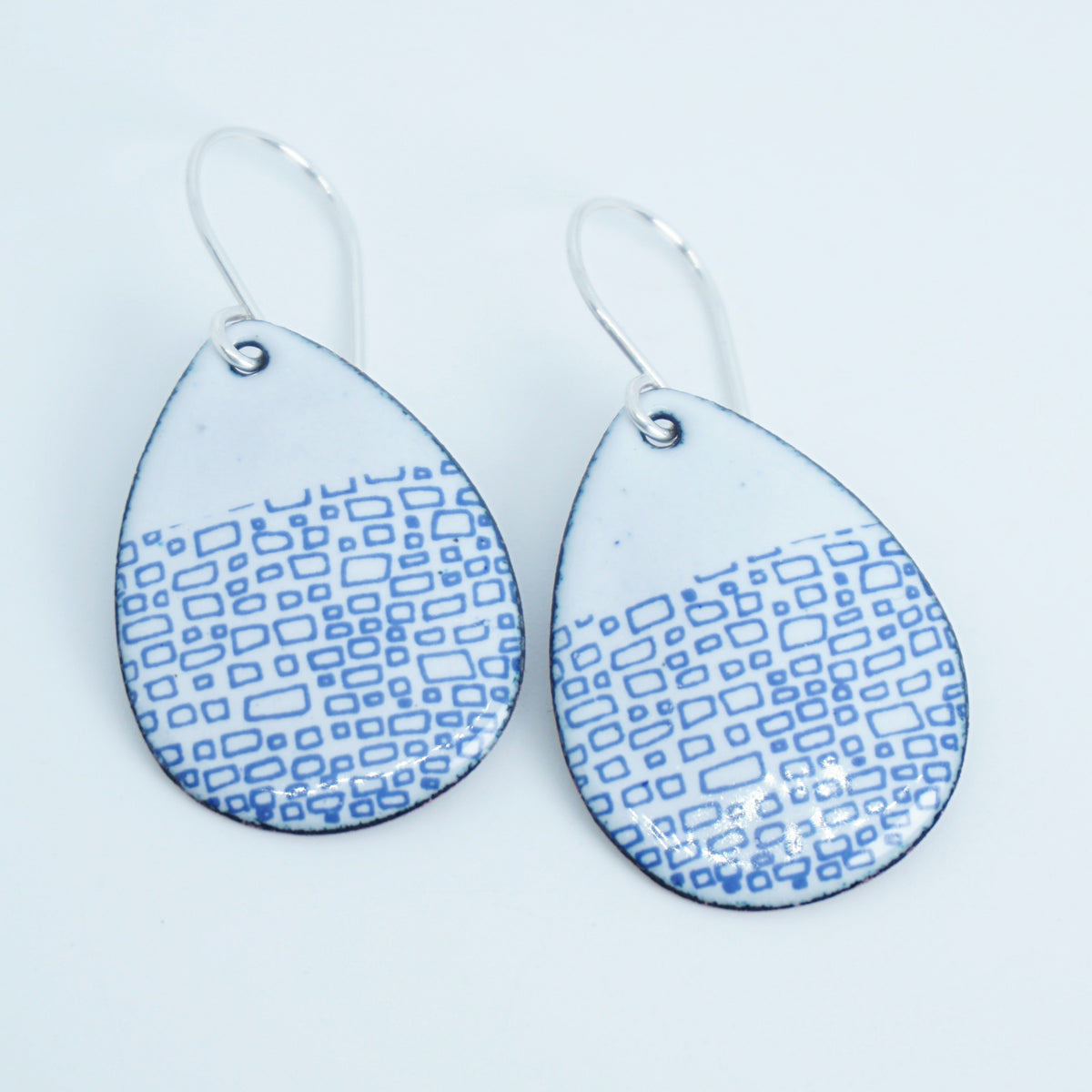 a pair of white enamel teardrop shaped earrings with blue accents, against a white background