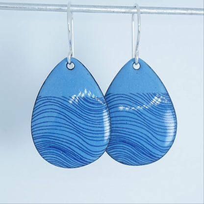 a pair of blue enamel teardrop shaped earrings with blue wavy line accents, against a white background