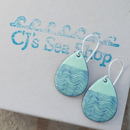 a pair of green enamel teardrop shaped earrings with blue wavy line accents, displayed on a gift box