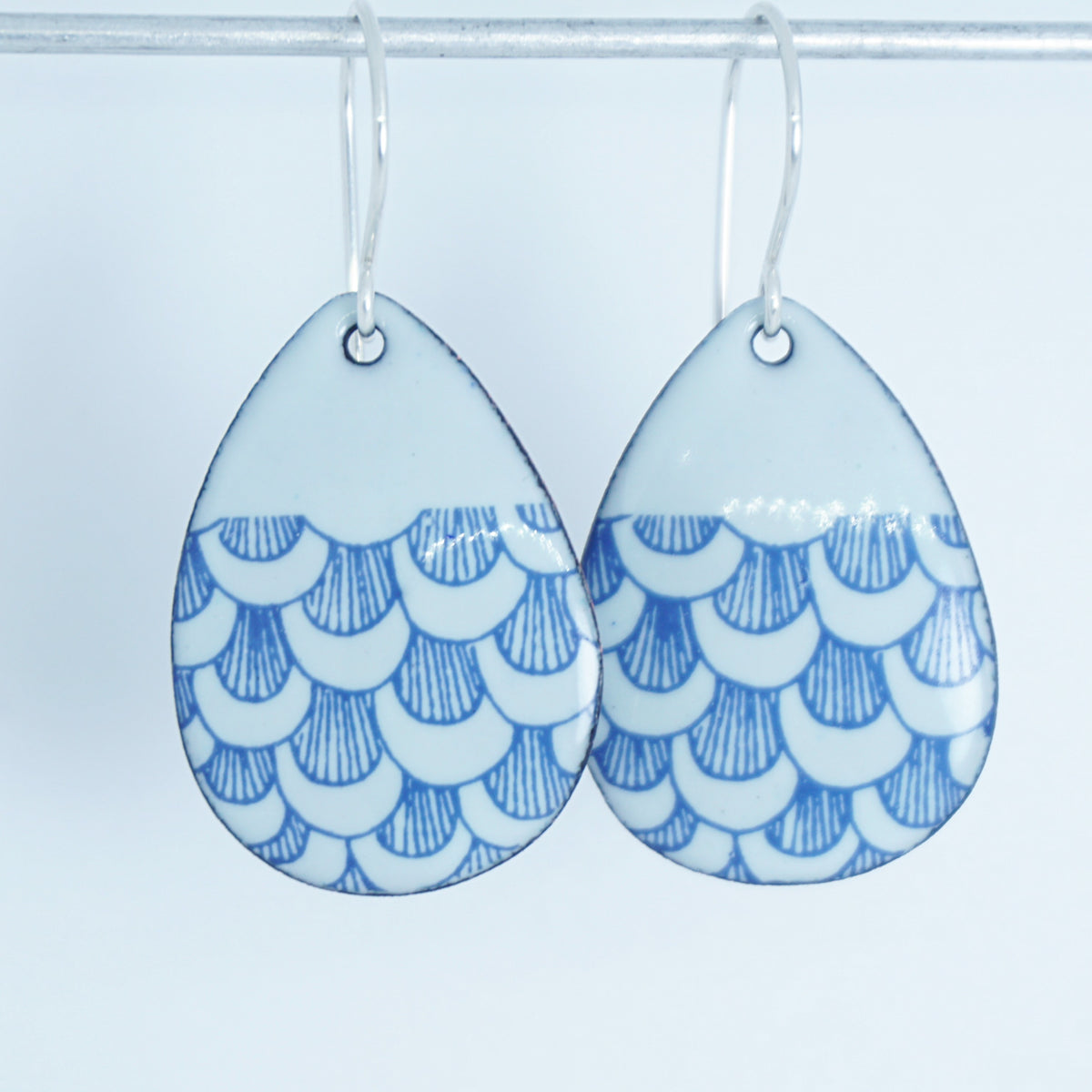 a pair of seafoam green enamel teardrop shaped earrings with blue fish scale accents, against a white background