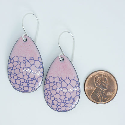 a pair of pink enamel teardrop shaped earrings with blue bubble accents, next to a penny for scale, against a white background