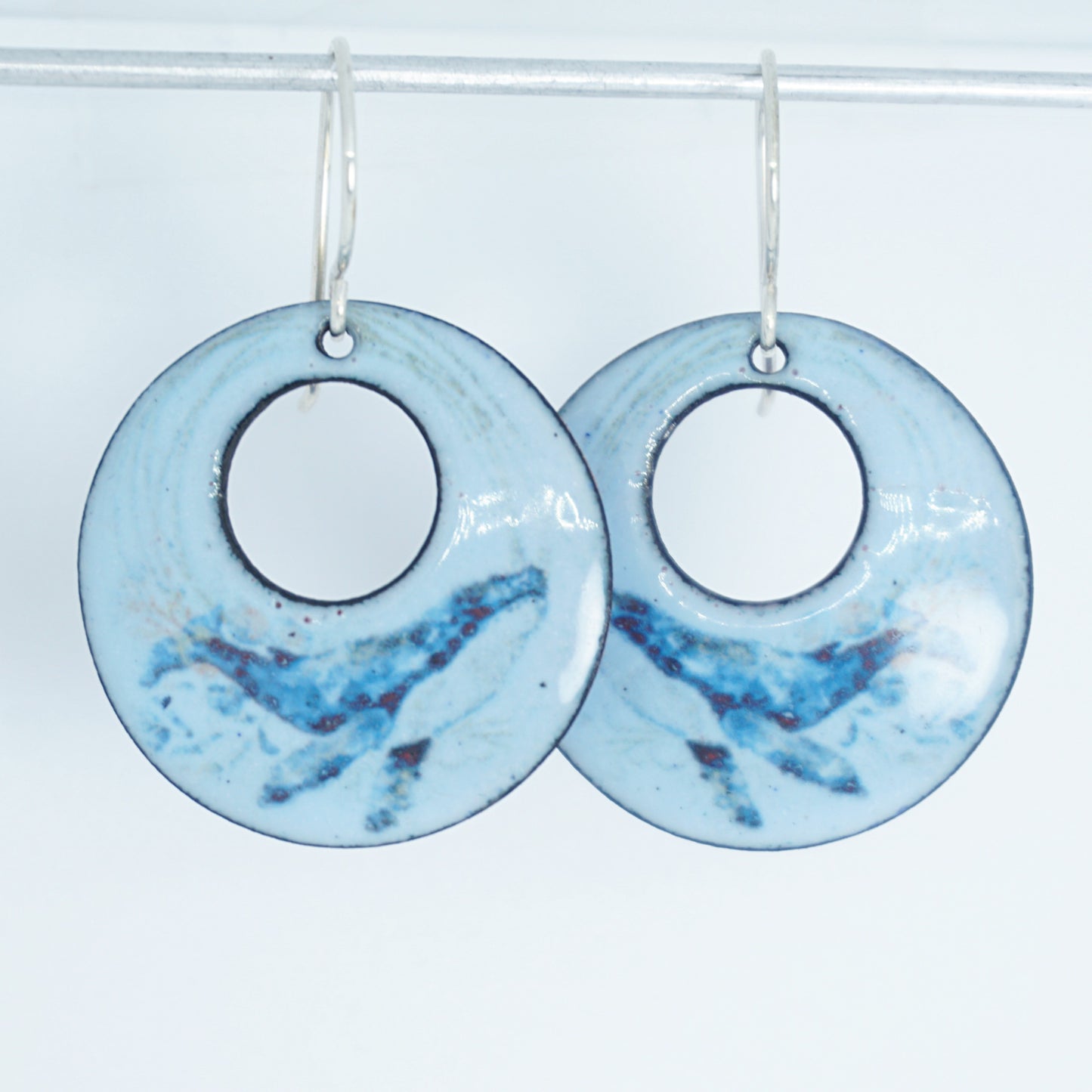 Pair of light blue circular earrings with a whale design on a white background