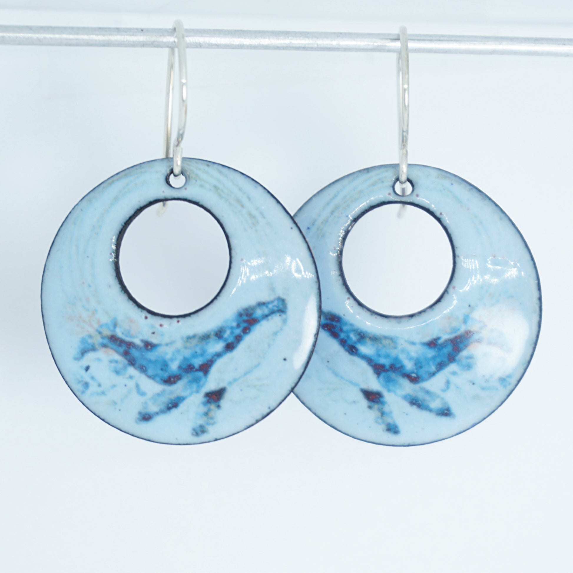 Pair of light blue circular earrings with a whale design on a white background