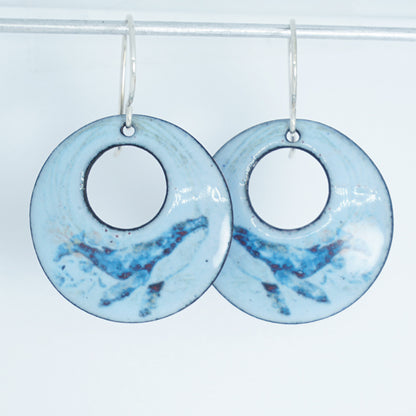 Pair of light blue circular earrings with a whale design on a white background