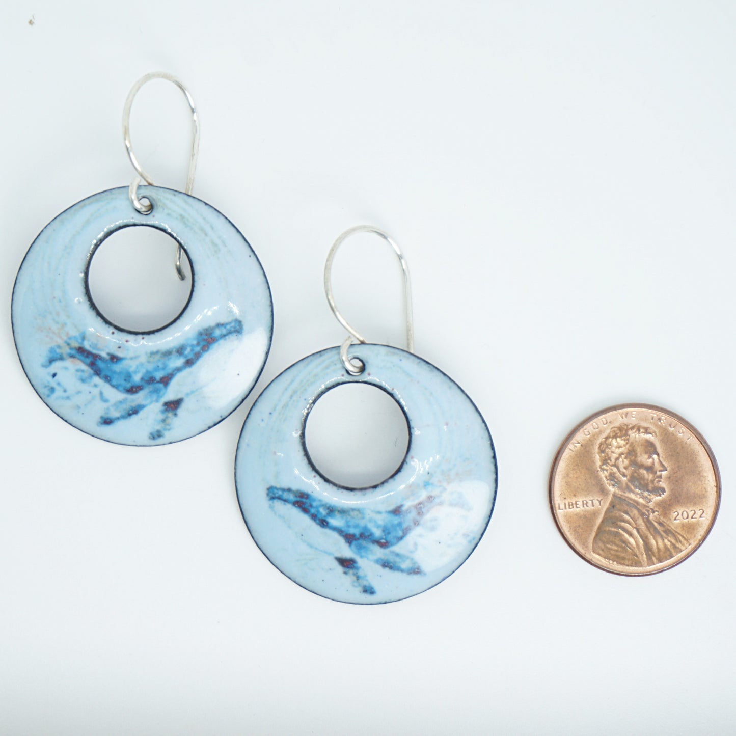 Pair of blue earrings with whale design with a penny for scale on a white background