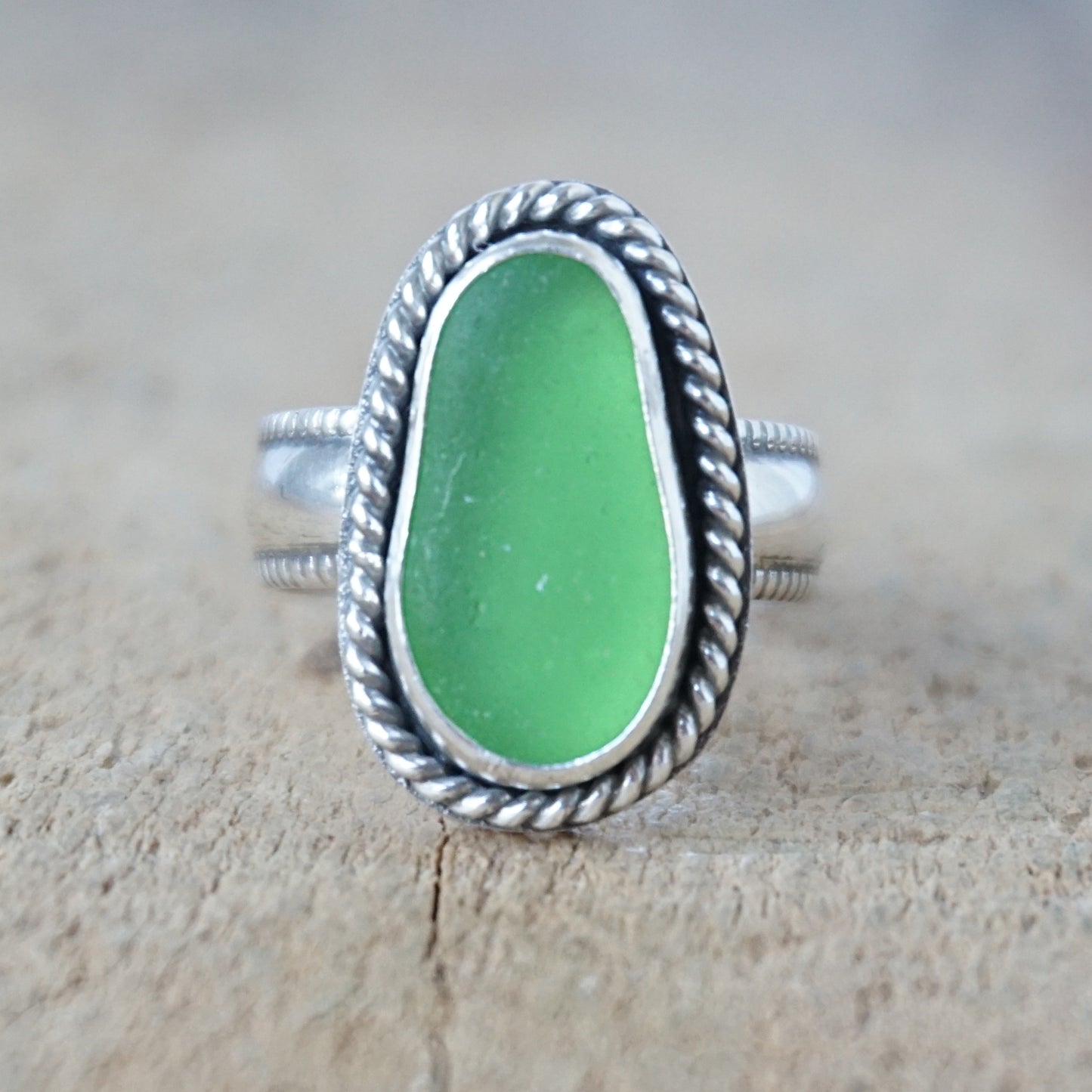 green sea glass ring with a decorative trim on a wooden background