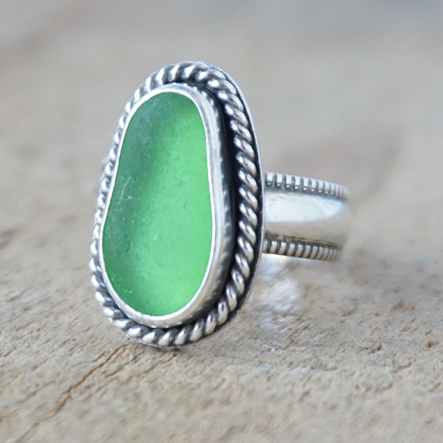 green sea glass ring with a decorative trim on a wooden background