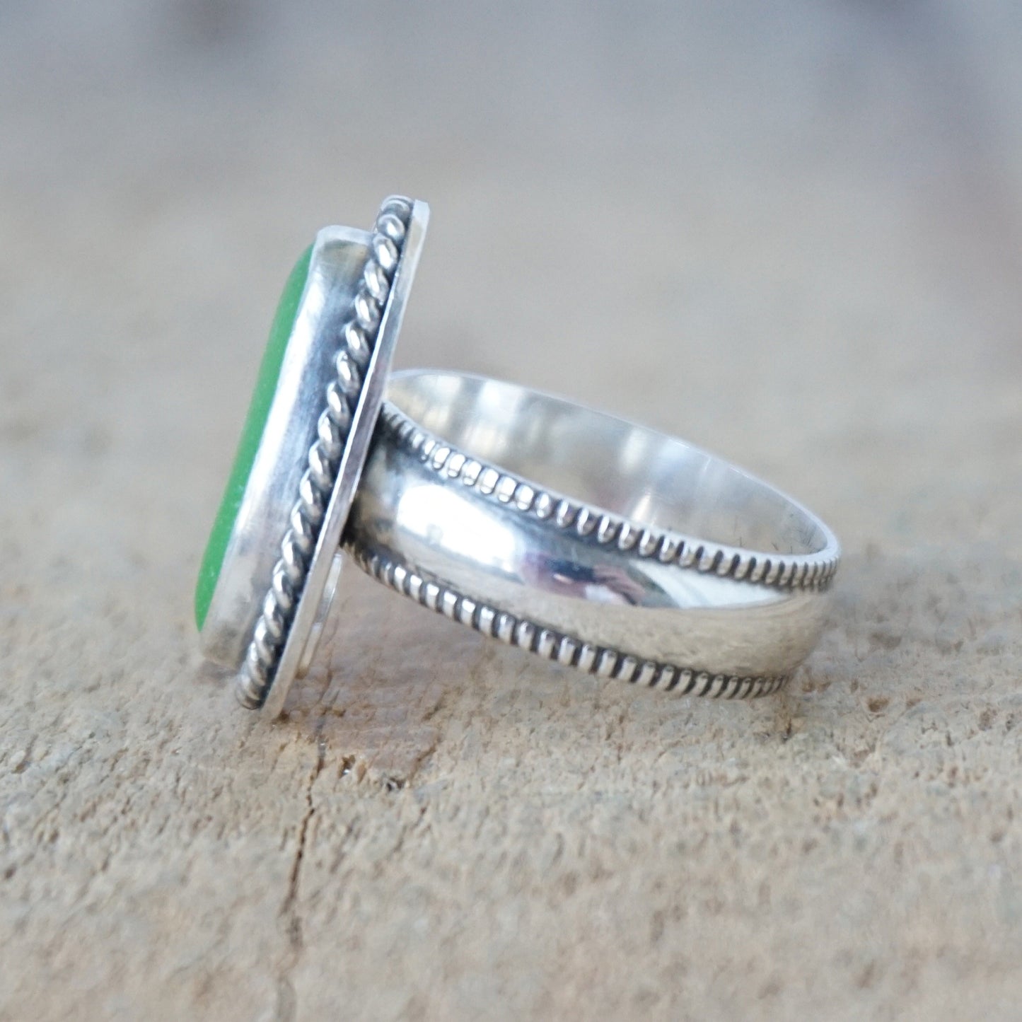 side view of a green sea glass ring with a decorative trim on a wooden background