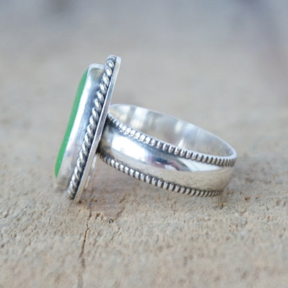 side view of a green sea glass ring with a decorative trim on a wooden background