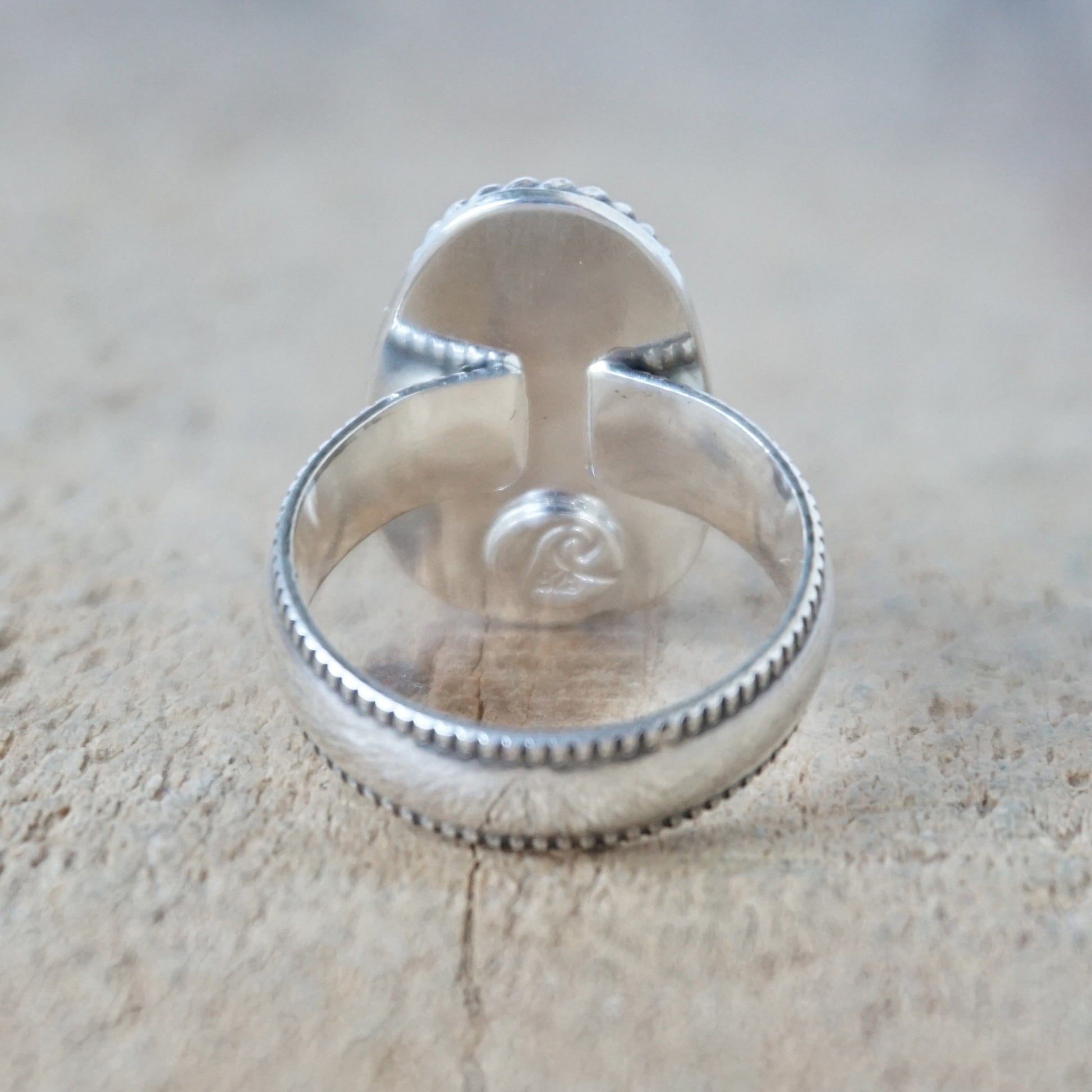 back view of a green sea glass ring with a decorative trim on a wooden background