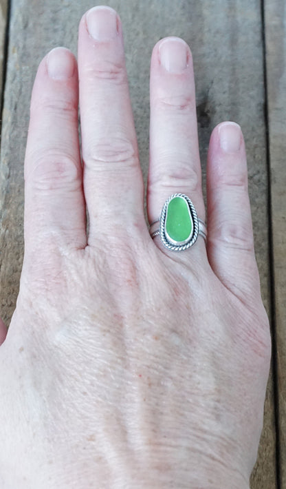 hand wearing a green sea glass ring with a decorative trim on a wooden background