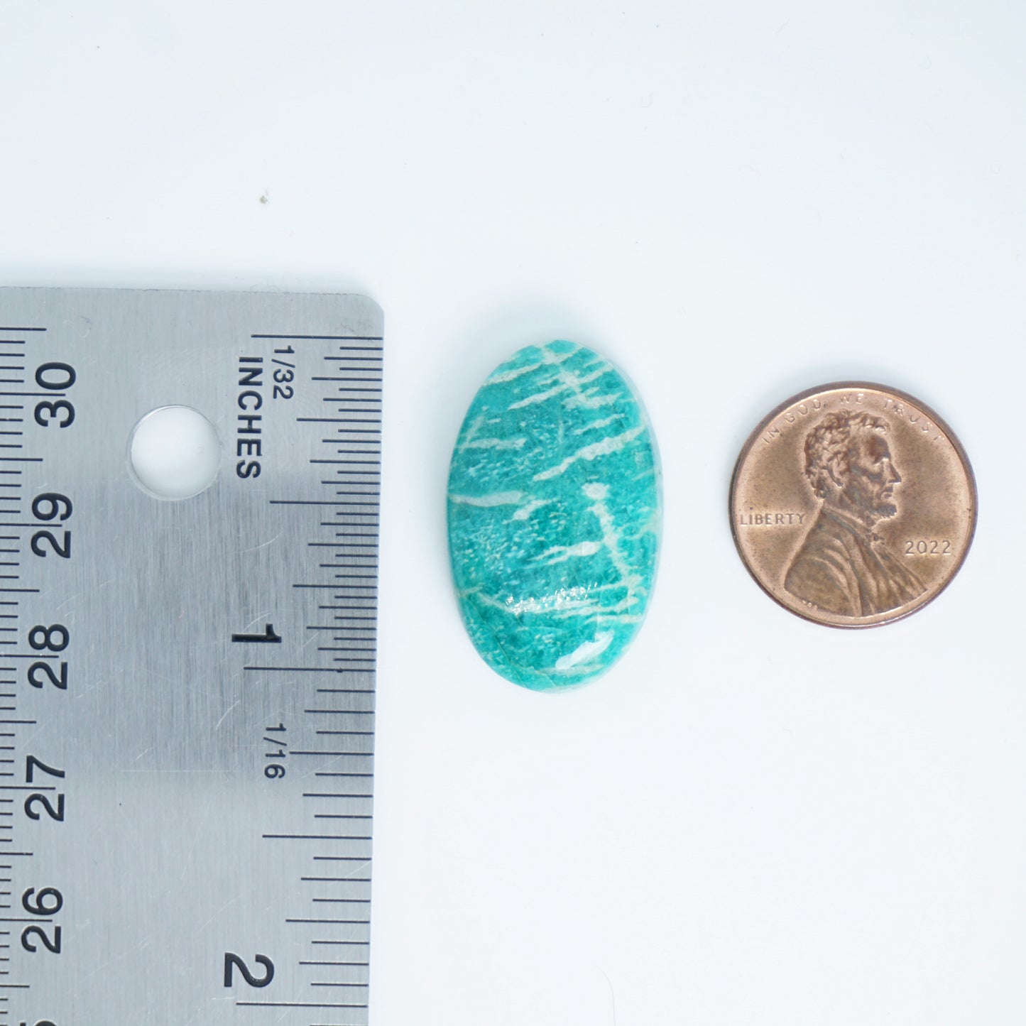 teal green stone with white veins next to a ruler and penny for size comparison on a white background