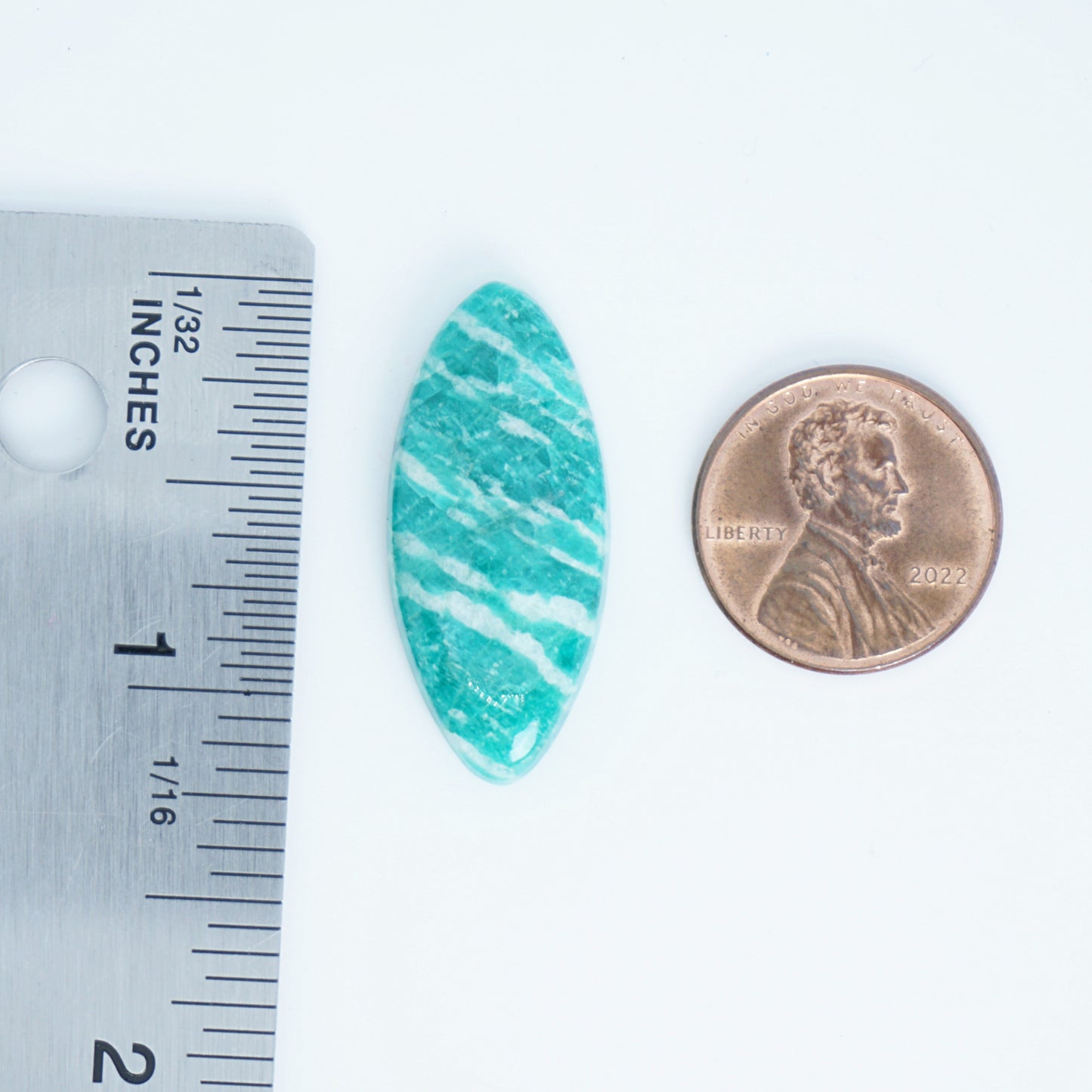 Turquoise stone with white stripes next to a penny and ruler for size comparison on a white background