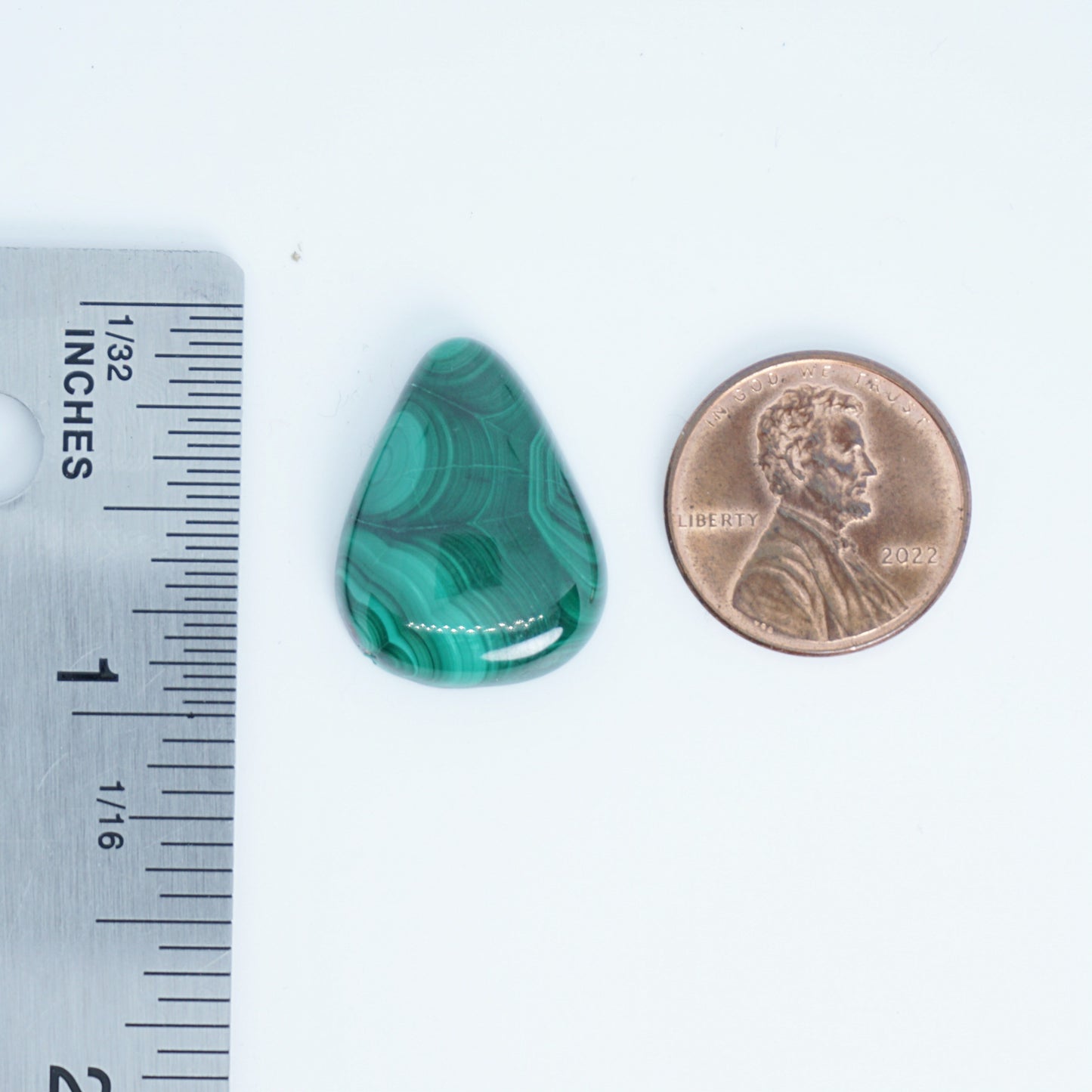 Green stone next to a penny and ruler for size comparison on a white background