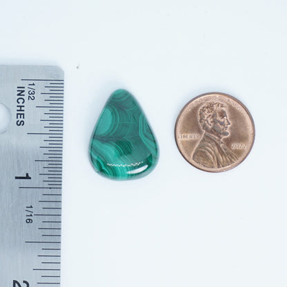 Green stone next to a penny and ruler for size comparison on a white background