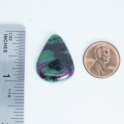 Teardrop-shaped green and purple stone next to a penny and ruler for scale on a white background
