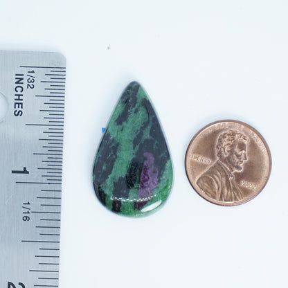 Teardrop-shaped green and black stone next to a penny and ruler for size comparison on a white background.