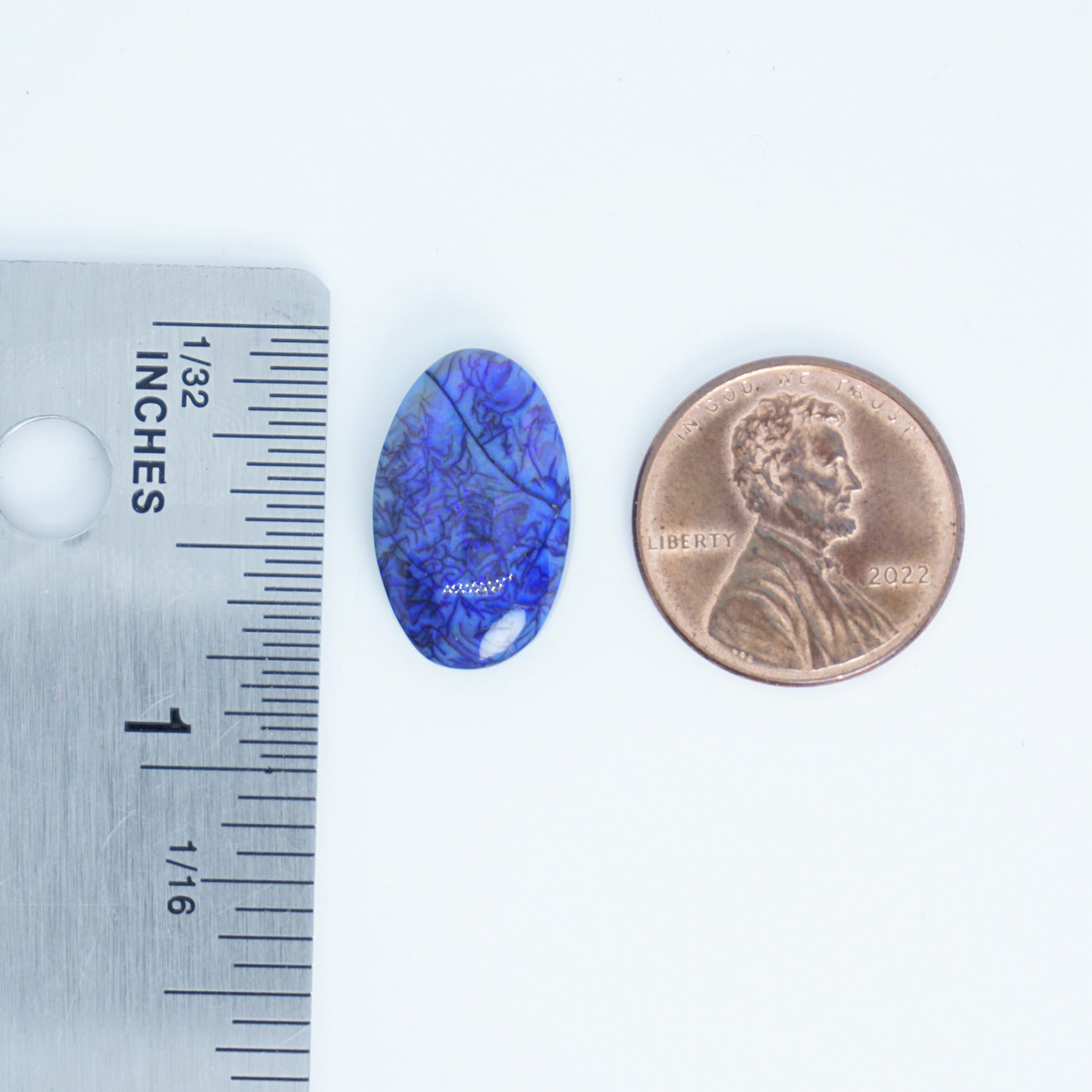 Blue oval stone next to a penny and ruler for size comparison on a white background