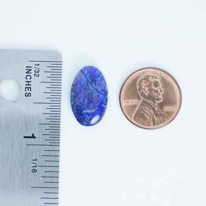 Blue oval stone next to a penny and ruler for size comparison on a white background