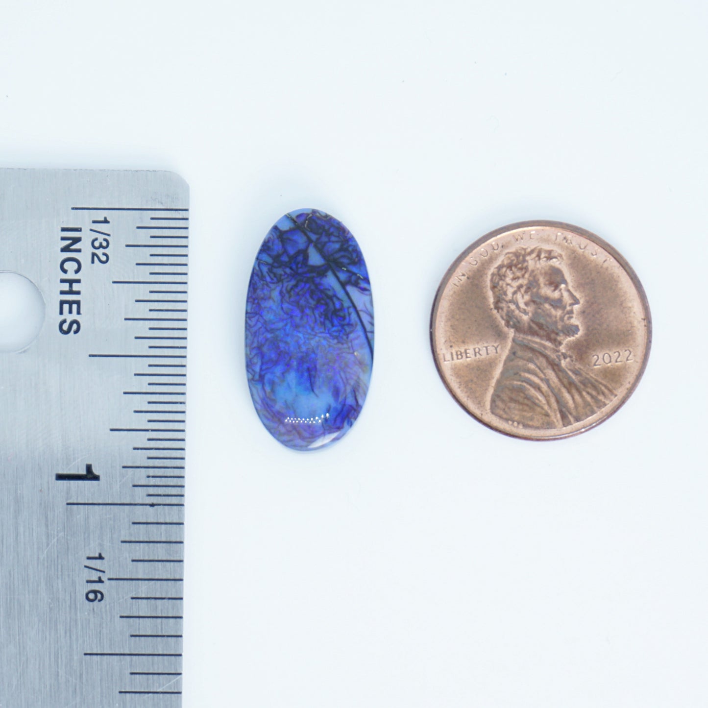Blue oval stone next to a penny and ruler for size comparison on a white background