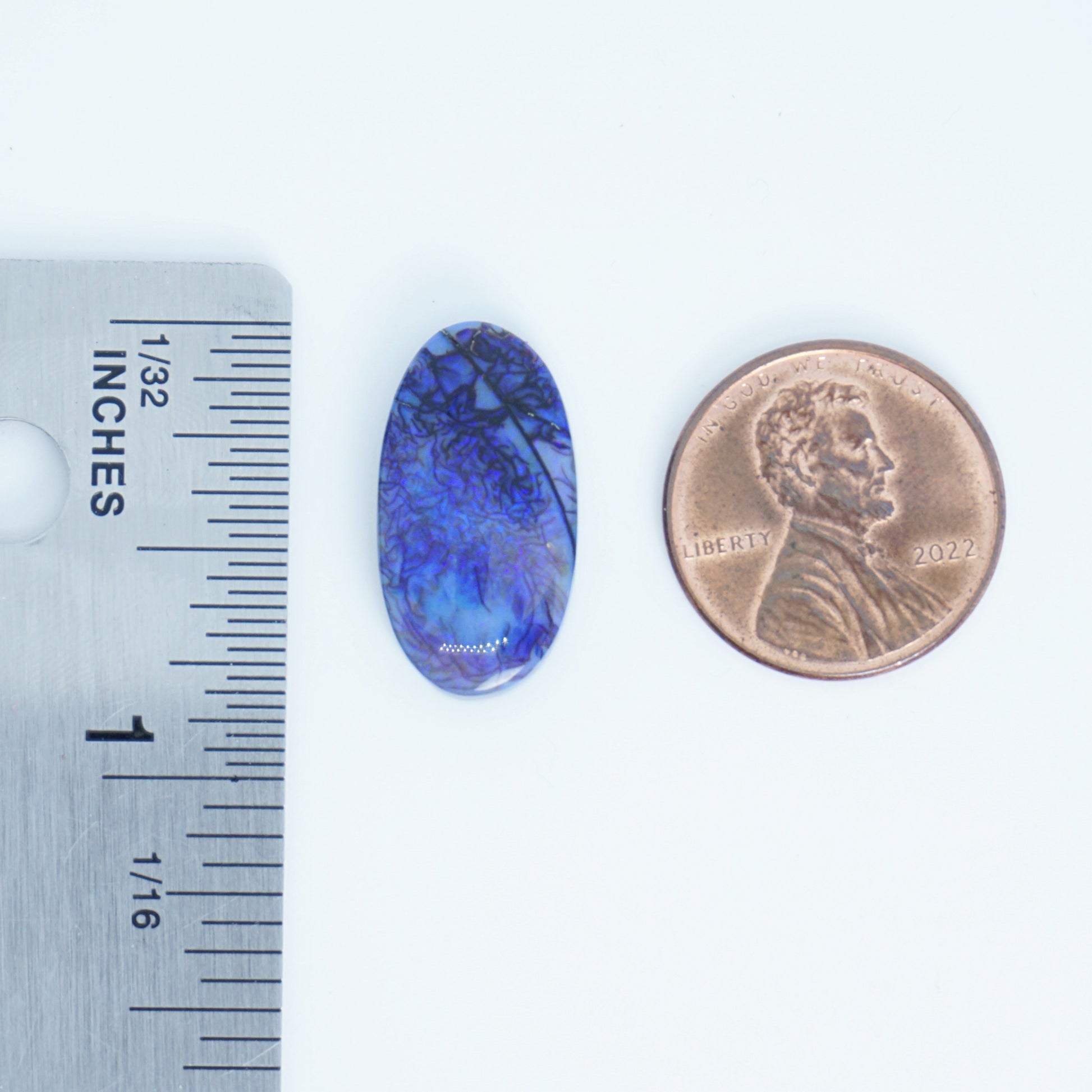 Blue oval stone next to a penny and ruler for size comparison on a white background