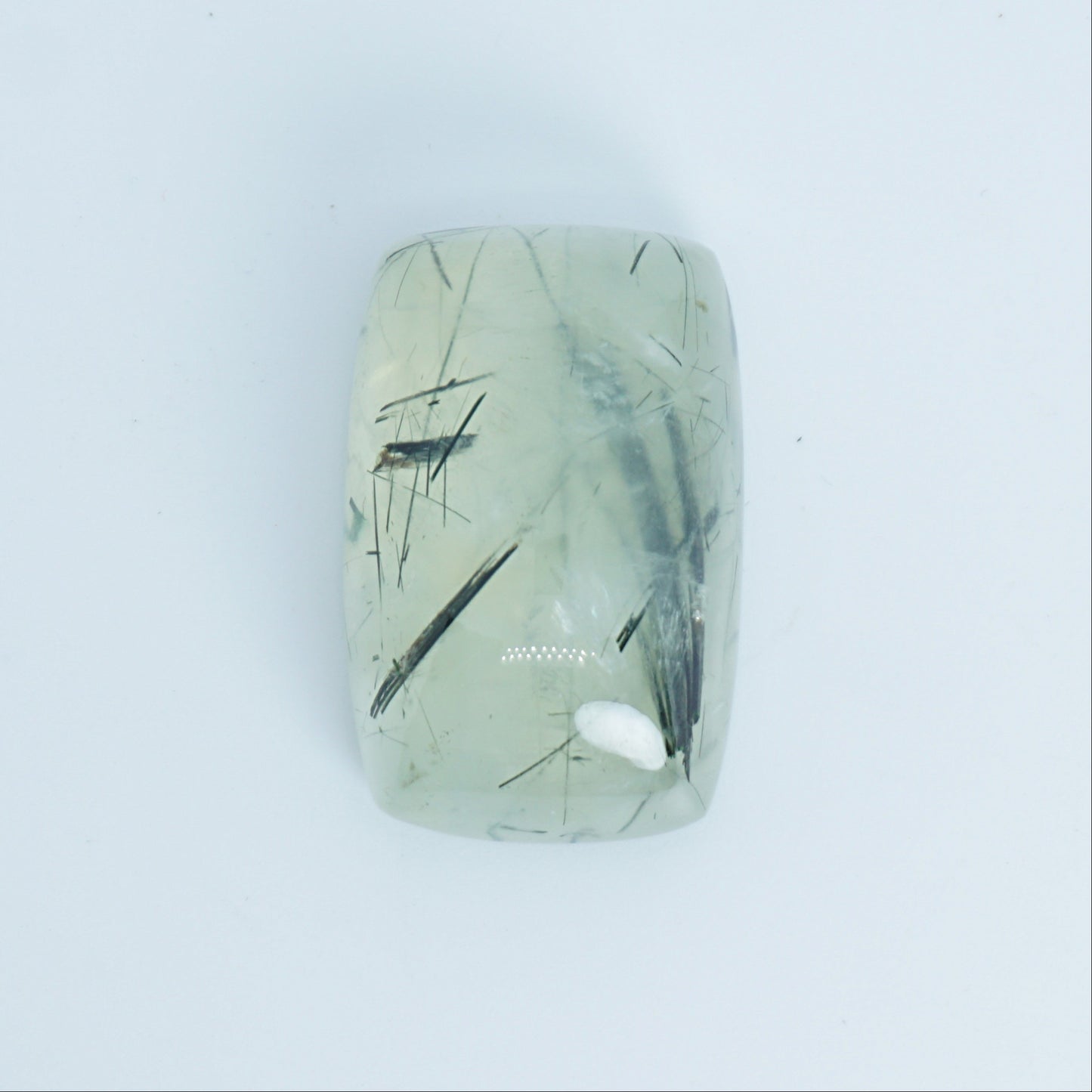Rectangular green prehnite stone with black markings on a light blue background