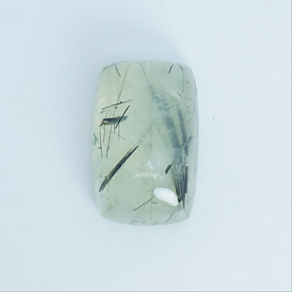 Rectangular green prehnite stone with black markings on a light blue background