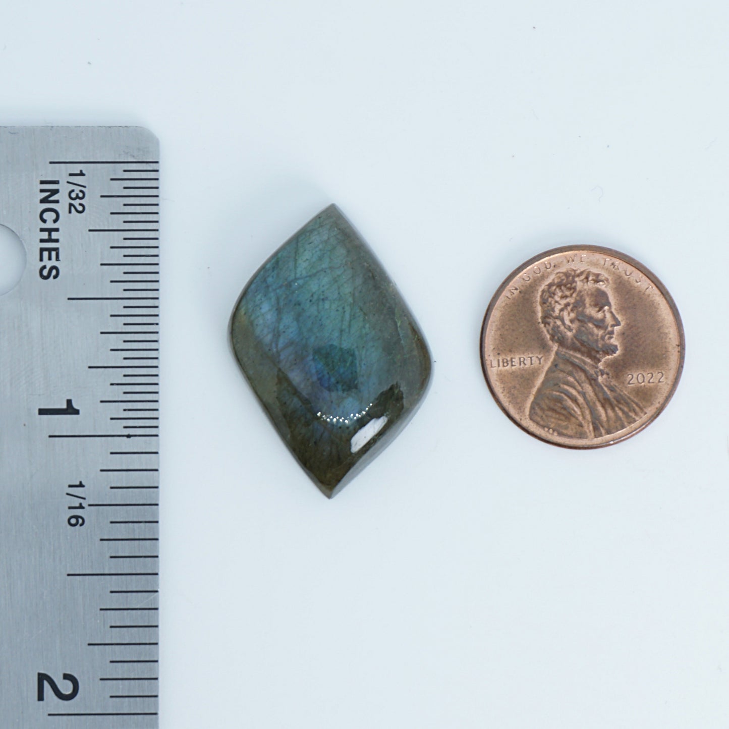 Labradorite stone next to a penny and ruler on a white background
