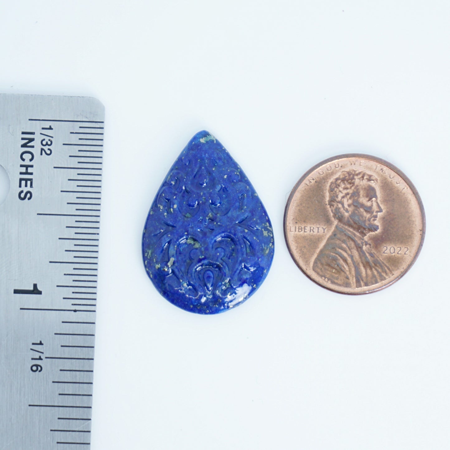 blue lapis cabochon with carved surface available for custom jewelry next to a penny and ruler for scale on a white background