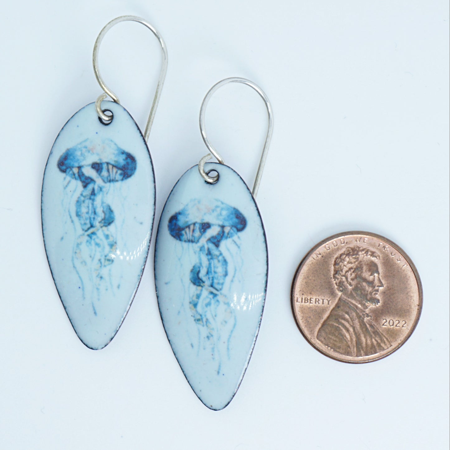 teardrop-shaped earrings with jellyfish design next to a penny for scale on a white background