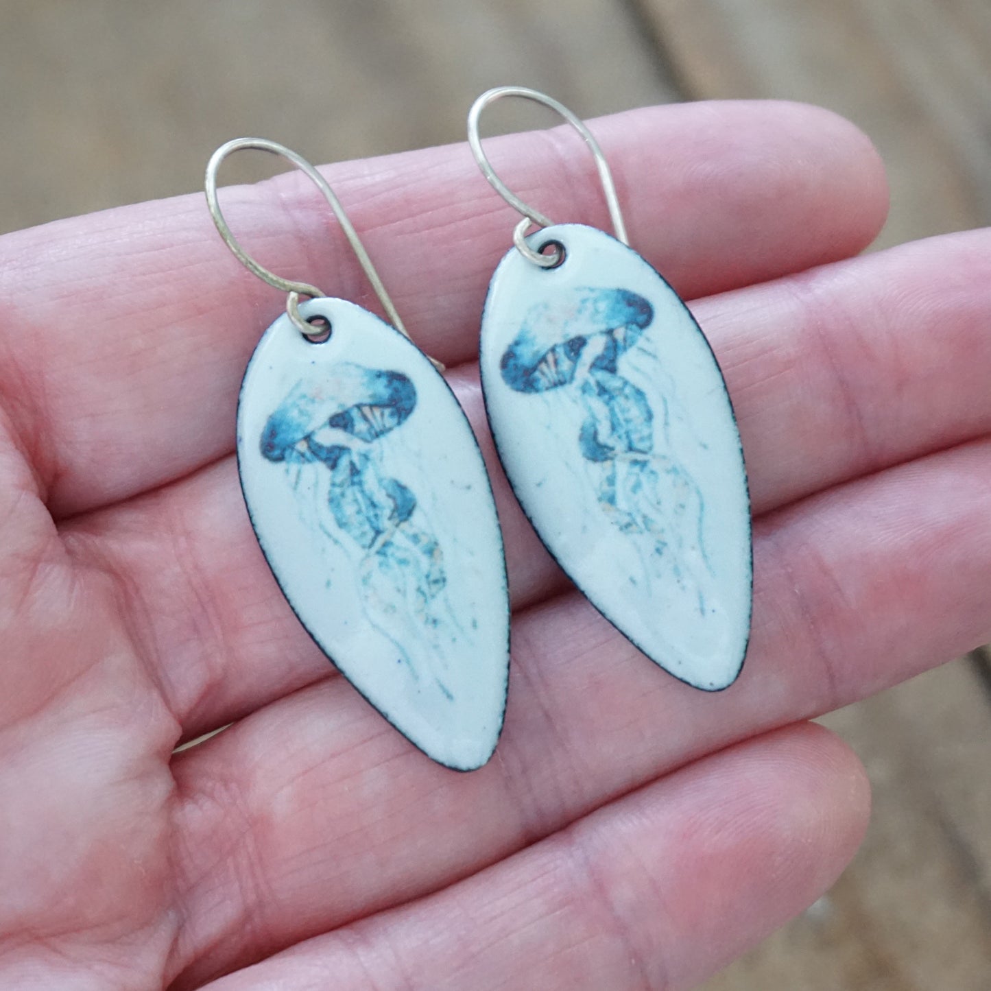 Earrings with jellyfish design held in a hand against a blurred background