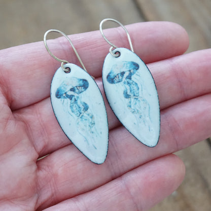 Earrings with jellyfish design held in a hand against a blurred background