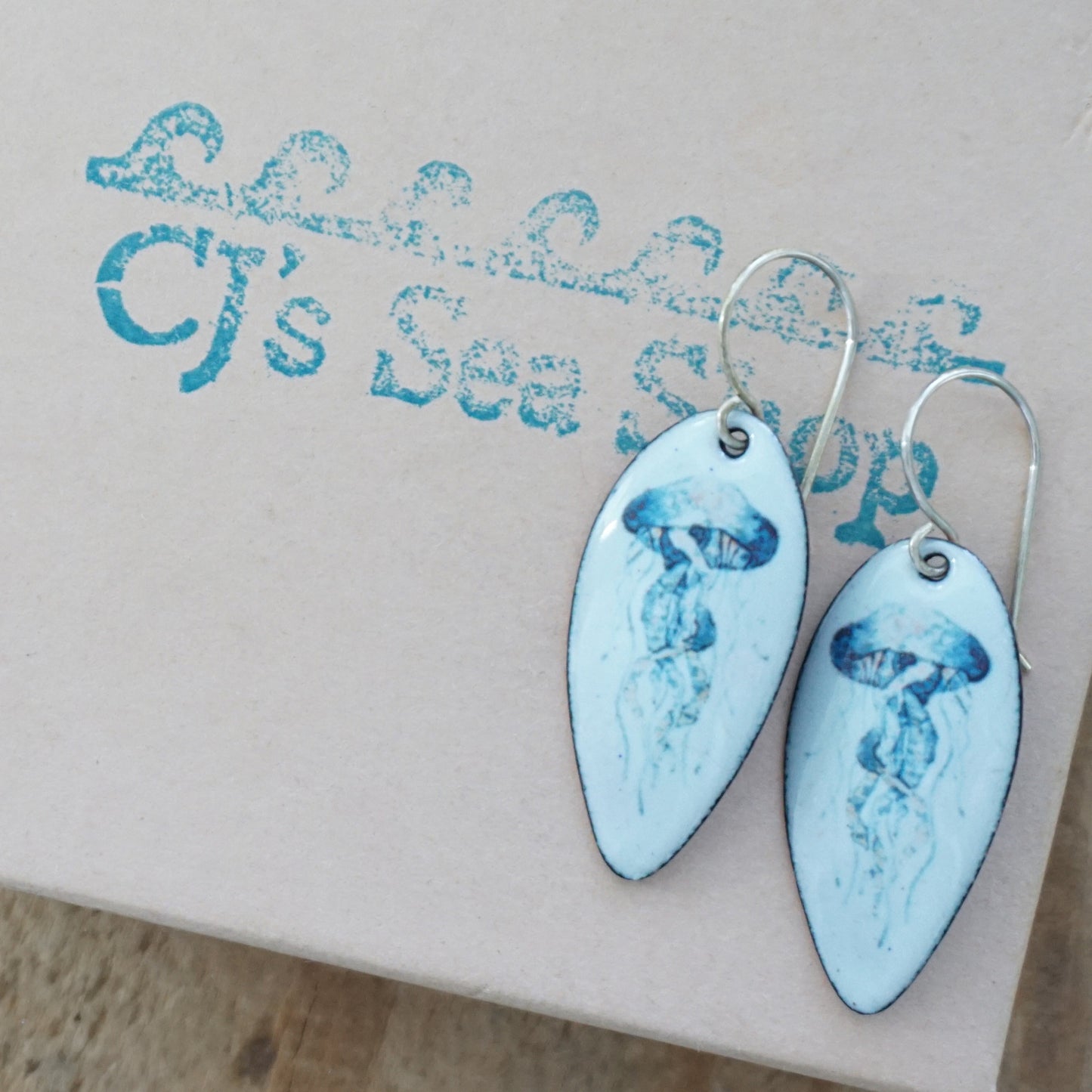 seafoma green teardrop-shaped earrings with a jellyfish desing on a gift box