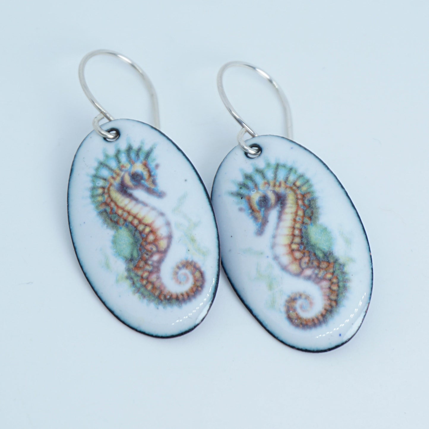 Oval-shaped earrings with seahorse designs on a white background