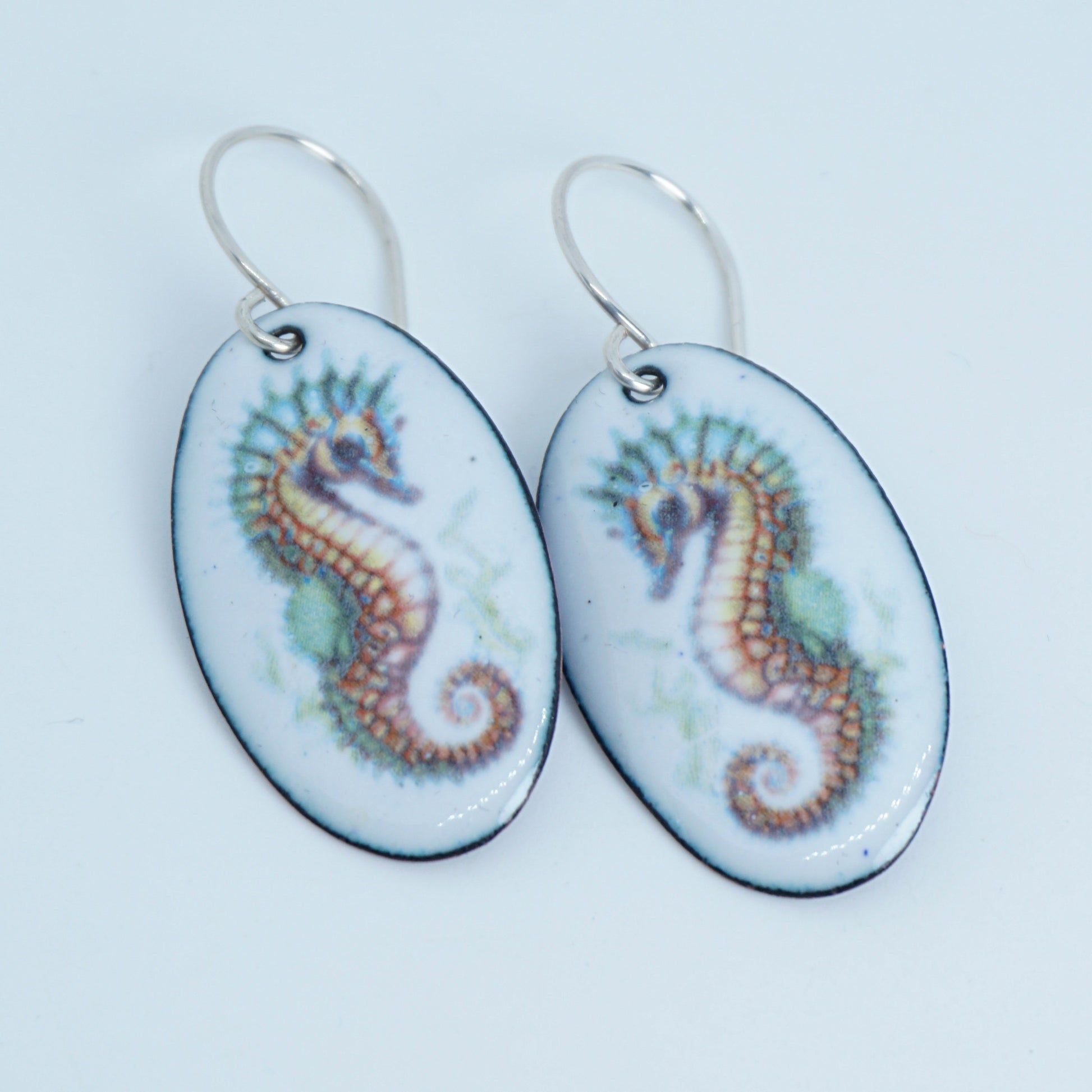 Oval-shaped earrings with seahorse designs on a white background