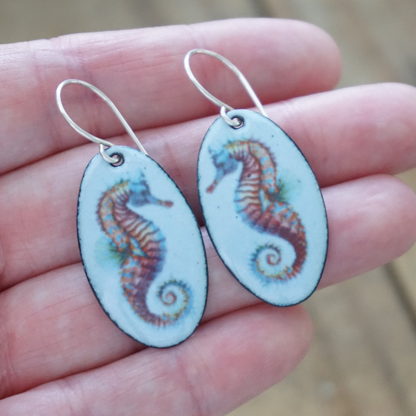 Colorful seahorse earrings held in a hand with a blurred background