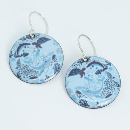 Pair of light blue earrings with a sea life design on a white background